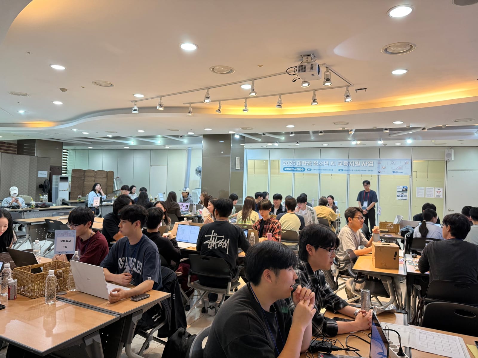 팀별 테이블에 앉은 멘토들이 앞쪽 발표를 듣고 있다