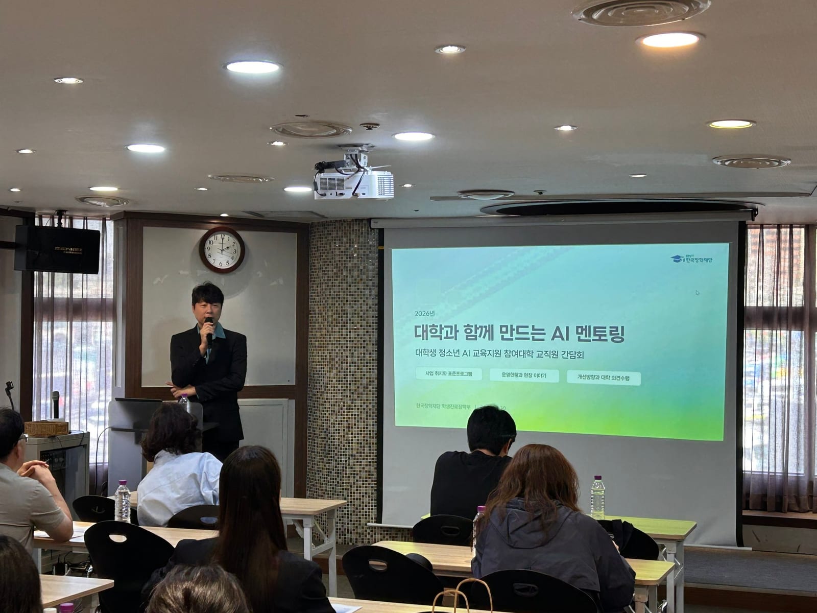 간담회장 전경 — 화면에 "대학과 함께 만드는 AI 멘토링" 표지가 떠 있고 대학 담당자들이 자리에 앉아 있다